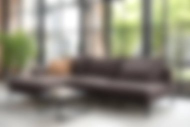 Sıcak ve cezbedici modern bir oturma odasında geniş pencerelere karşı rahat, kahverengi bir kanepe sergileniyor, doğal ışığı artırıyor ve sakin bir atmosfer için yeşillik sunuluyor..