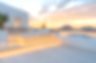 Bu görüntü, dinlenme ve sükuneti çağrıştırmak için ideal bir havuz ve manzara arka planının yer aldığı modern bir açık hava salonundan huzurlu bir gün batımı görüntüsü yakalıyor..