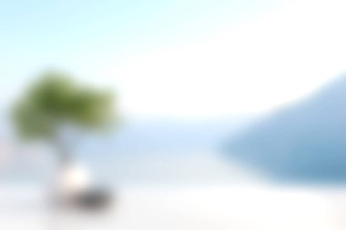 Suyun ve dağların bulanık arkaplanına sahip bir ağacın yer aldığı sakin ve huzurlu bir manzara. Sakinlik ve rahatlama hissi uyandırmak için mükemmel..