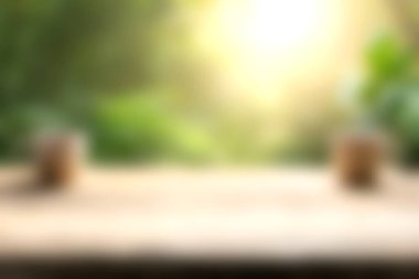 Yumuşak güneş ışığıyla aydınlatılmış bulanık ahşap bir masanın bulunduğu sakin bir açık hava sahnesi, yemyeşil, sakin ve taze bir atmosfer yaratıyor..