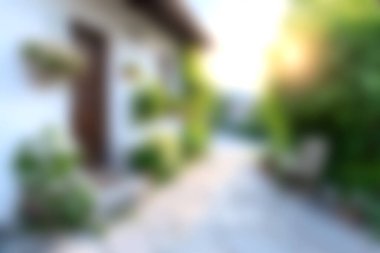 Sakin bir bahçe yolunda canlı yeşillik ve yumuşak güneş ışığıyla çevrili rahat bir ev sergileniyor. Barışçıl yaşamın ve açık hava güzelliğinin mükemmel bir temsili..