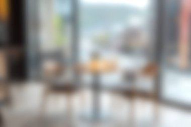 Büyük bir pencerenin yanında şık sandalyeler ve masa bulunan rahat bir kafe, dinlenme ve toplantı için sıcak ve davetkar bir atmosfer yaratıyor..