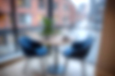 Büyük bir pencerenin yanında şık sandalyeler ve masa bulunan rahat bir kafe, dinlenme ve toplantı için sıcak ve davetkar bir atmosfer yaratıyor..