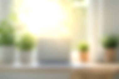 Parlak ve davetkar bir çalışma alanı. Etrafı yeşil bitkilerle çevrili bir dizüstü bilgisayar. Pencere kenarındaki ahşap masa üzerinde..