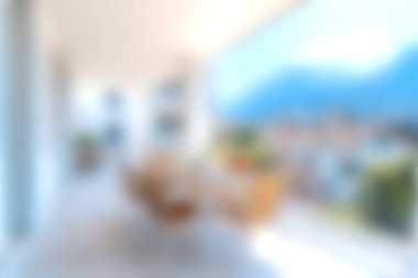 Bu resim, rahat koltukları olan modern bir balkon ve berrak gökyüzünün altındaki uzak dağların çarpıcı manzarasını sergiliyor..