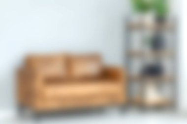 Rahat bir oturma odasında modern bir kitaplıkla eşleştirilmiş şık, kahverengi bir kanepe var. Hoş bir atmosfer için yeşil ve dekoratif unsurlar sergiliyor..