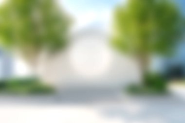 Bu sakin görüntü, parlak mavi gökyüzünün altında, mimari veya yaşam tarzı temalar için ideal, yemyeşil ağaçlar tarafından çerçevelenmiş bulanık bir ev cephesine sahiptir..