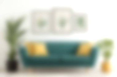 Yeşil bitkiler ve modern sanat eserleriyle çevrili sarı yastıklarla süslenmiş zarif bir deniz mavisi kanepenin olduğu rahat bir oturma odası. Rahatlamak için davetkar bir ortam..