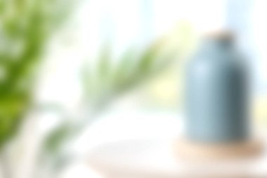 Yumuşak odaklı bir mavi seramik vazo, parlak bir ortamda yemyeşil ile çevrili bir yüzeyde oturur. Huzurlu ve davetkar bir atmosfer yaratır. Ev dekorasyonu için mükemmel..