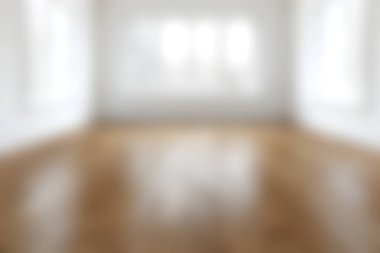 Bu resim parlak ve ferah, ahşap zeminli ve geniş pencereli boş bir oda içeriyor, doğal ışıkla dolu huzurlu bir atmosfer yaratıyor..