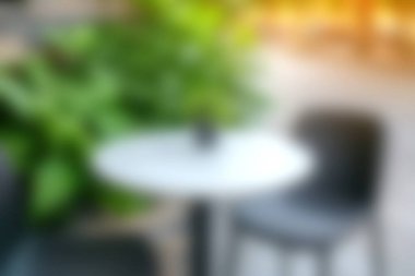 Yeşilliklerle çevrili yuvarlak masa ve sandalyenin olduğu rahat, modern bir kafe sahnesi. Yumuşak bulanık arka plan dinlenmek için davetkar bir atmosfer yaratır..