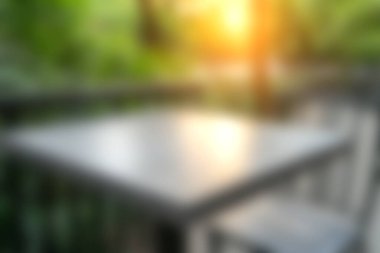 Sıcak bir günbatımı parıltısıyla aydınlatılmış yumuşak odaklı bir masanın yer aldığı sakin bir açık hava sahnesi. Bereketli yeşillik huzurlu ortamı sarar, dinlenmek için sakin bir atmosfer yaratır..