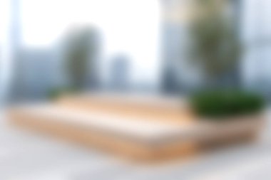 Ahşap bir güverte ve bereketli bitki düzenlemelerinin yer aldığı, kentsel bir ortamda rahatlamaya davetiye çıkaran, modern bir açık hava alanını gösteren yumuşak odaklı bir görüntü..