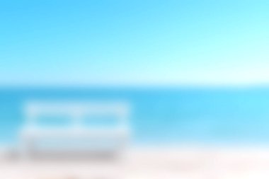 Ön planda beyaz bir bank olan sakin bir sahil sahnesi, engin mavi bir okyanus ve arka planda bulutsuz bir gökyüzü, rahatlama için mükemmel..