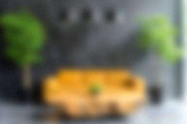 Gri bir duvara karşı yemyeşil bitkiler tarafından tamamlanmış parlak sarı bir kanepenin bulunduğu rahat, modern bir oturma odası, huzurlu bir atmosfer yaratıyor..