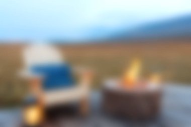 Parlayan bir ateş çukurunun yanında rahat bir sandalyenin olduğu açık hava sahnesi, akşam rahatlığı için mükemmel. Huzuru ve sıcaklığı yakalar.