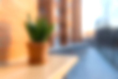 Bulanık bir görüntü modern bir balkon ve bir saksı bitkisini gün batımında şehir manzarasına karşı sergiliyor. Sıcak tonlar dingin bir atmosfer yaratır..