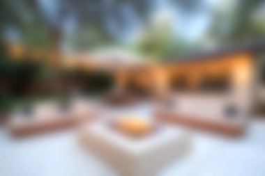 Bu resim, yumuşak akşam ışığı ile çevrili bir ateş çukuru ve büyük bir şemsiye içeren, rahatlama ve toplanma için mükemmel bir açık hava verandası sergiliyor..