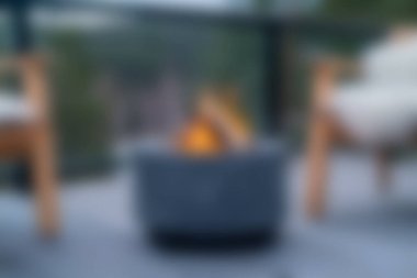 Modern sandalyelerle çevrili, yumuşak odaklı sıcak bir ateş çukurunun yer aldığı sakin bir açık hava sahnesi. Rahatlama ve sosyal etkinlikler için mükemmel..