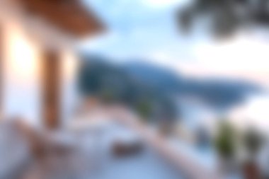 Gün batımında veranda mobilyalarının bulanık manzaralı güzel bir sahil manzarası. Bu huzurlu ortam, deniz kıyısından huzurlu bir kaçışı çağrıştırıyor..