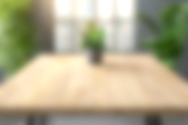 Orta süsü yeşil bir bitki olan ahşap bir masanın yumuşak odak noktası doğal ışıkla dolu parlak bir iç mekanda sakin bir atmosfer yaratıyor..