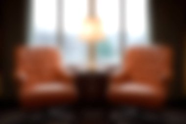 Bir lambanın yanında iki klasik sandalyenin olduğu sakin bir oturma odası, pencereden içeri ışık süzülen sıcak ve davetkar bir atmosfer yaratıyor..