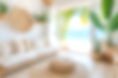 Bu görüntü, plaja tepeden bakan tropikal dekor elementleriyle aydınlık ve davetkar bir oturma odasını, rahatlama ve rahatlama için ideal sakin bir atmosfer yaratıyor..