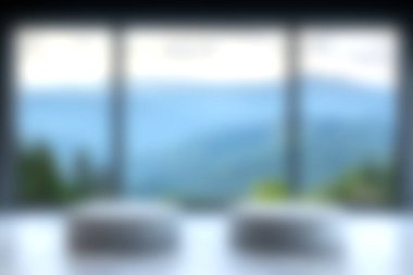 Geniş bir pencereden görülen sakin bir dağ manzarası keşfedin, rahatlatıcı bir atmosfer yaratan yumuşak odaklı elementler içerir..