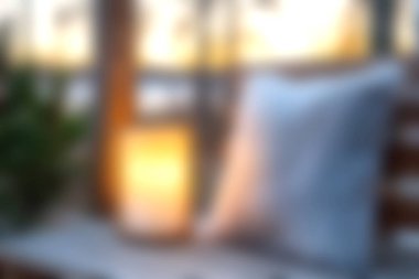 Ahşap bir yüzeyde yumuşak dekoratif bir yastığın yanında parlayan bir ışık kaynağının olduğu sakin bir akşam sahnesi, rahatlama ve sıcaklık uyandırmak için mükemmel..