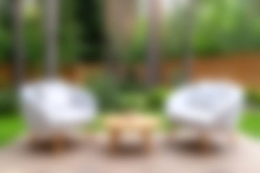 İki beyaz sandalye ve bir ahşap masa içeren sakin bir açık hava oturma alanı, yemyeşil bir ortamda yerleşmiş, rahatlamak ve doğada rahatlamak için mükemmel..