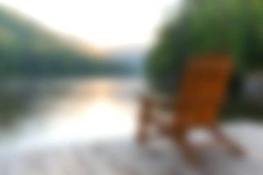 Huzurlu sabahlar, sakin bir gölün kenarındaki ahşap sallanan sandalyenin yumuşak odaklı görüntüsüyle, rahatlama ve huzur uyandırmak için mükemmel..