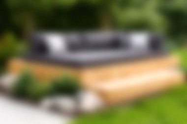 Yeşilliklerle çevrili ahşap bir güvertede modern bir açık hava kanepesi. Rahatlamak ve şık bir şekilde dışarıda yaşamak için mükemmel..