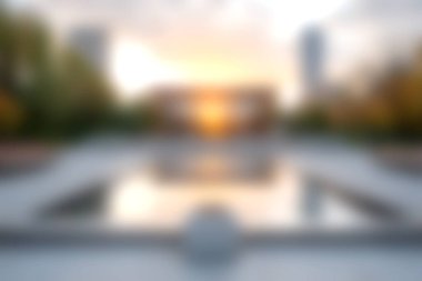 Renkli ağaçlar ve modern binalarla çerçevelenmiş, sakin ve sakin bir atmosfer yaratan bir şehir parkındaki sakin suyun üzerinde güzel bir günbatımı yansıtıyor..