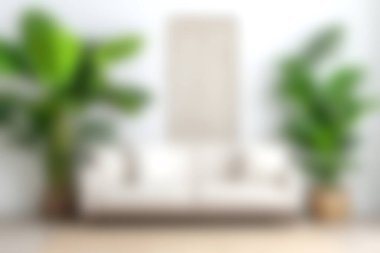 Huzurlu ve davetkar bir oturma odasında beyaz bir kanepe sergileniyor. Kapalı alandaki bitkilerle çevrili. Ev dekorasyonunda mükemmel bir konfor ve minimalizm karışımı sunuyor..