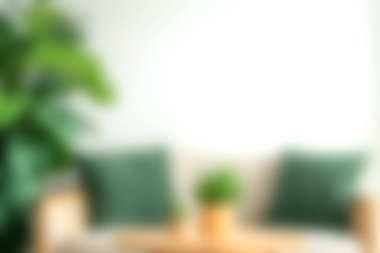 Açık renkli bir kanepede, ahşap bir masada küçük bir saksı bitkisi olan yumuşak yeşil yastıkların olduğu rahat bir oturma odası sahnesi. Parlak ve zarif atmosfer rahatlamak için bir karşılama alanı yaratır..