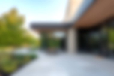 A modern architectural entrance surrounded by lush landscaping, featuring a smooth patio and bright sunlight, creating a serene outdoor atmosphere.