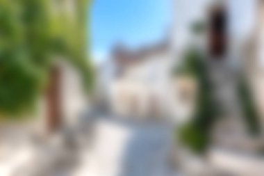 Explore a picturesque cobblestone street lined with charming white buildings and lush green plants under a bright blue sky. Perfect for travel enthusiasts.