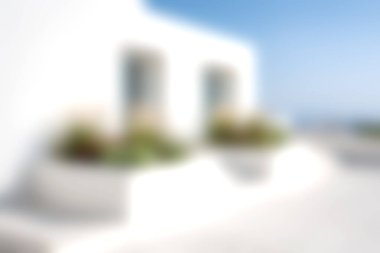 Bu yumuşak odak görüntüsü, çiçek saksılarıyla bezenmiş minimalist beyaz bir yapıyı mavi gökyüzüne yansıtıyor, sükunet ve yaz atmosferini çağrıştırıyor..