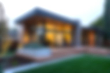 Modern mimari, tasarım unsurları ve sükuneti artıran bulanık bir bahçe arka planına sahip çağdaş bir evin görsel olarak çarpıcı bir görüntüsü..