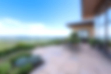 Yumuşak odaklı bir görüntü, açık gökyüzünün altında canlı bir manzaraya bakan modern bir terası gösteriyor. Rahatlamak ve açık havada yaşamak için mükemmel..