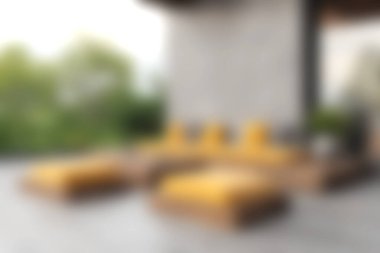 Konforlu bir açık hava oturma alanı, rahatlatıcı ve sakin bir atmosfer için verimli yeşilliklerle çevrili ahşap mobilyalar üzerinde parlak sarı yastıklar içerir..