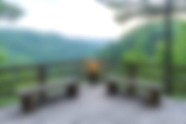 Yeşillik ve arka planda dağlarla çevrili ahşap bankların yer aldığı sakin bir bakış açısı, rahatlama ve doğa fotoğrafçılığı için mükemmel..