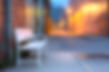 Yumuşak, bulanık bir sokak resmi, sıcak, parlayan ışıklarla çevrili bir bankta, yalnızlık ve huzur hissi uyandıran sakin bir şehir atmosferi yaratıyor..