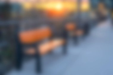 Gün batımında şehir parkındaki bankların huzurlu ve bulanık görüntüsü, akşam atmosferinde sakinlik ve rahatlığı çağrıştırıyor. Huzurlu havanın tadını çıkar..