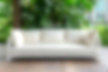 Modern beyaz bir kanepe, bereketli yeşilliklerle çevrili, kapalı bir alanda rahat bir oturma seçeneği sunuyor, sakin ve şık bir atmosfer yaratıyor..