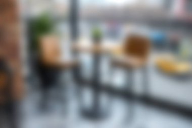 Bar tabureleri ve saksı bitkileriyle dolu küçük bir masa içeren rahat, modern bir kafe. Rahatlama ve sosyal etkileşim için davetkar bir atmosfer yaratıyor..