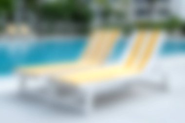 Işıl ışıl mavi yüzme havuzunun yanındaki iki rahat sarı dinlenme yeri güneşli bir tatil köyünde rahatlama ve rahatlama için mükemmel bir sahne oluşturur..