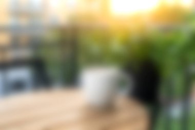 Bir ahşap masa, parlayan güneş ışığı arkaplanı ve gevşemek ve keyif almak için mükemmel yeşil bitkiler içeren sakin bir sabah sahnesi..