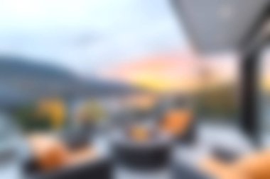 Konforlu bir açık hava verandası sergileniyor. Yumuşak, sıcak ışıkları olan, şık mobilyaları aydınlatan, rahatlatıcı ve davetkar bir atmosfer yaratan çarpıcı bir gün batımı manzarası..