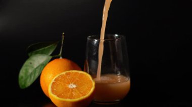 Siyah zemin üzerinde taze portakal suyu ve buz olan bir bardak.